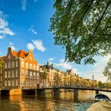 Un día perfecto para viajar a Ámsterdam: casas históricas junto a un canal, puentes y barcas bajo un cielo azul.