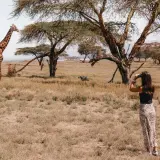 Una mujer observa una jirafa en la sabana, una escena típica de un viaje a Kenia.