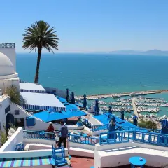 Vista de un puerto deportivo y el mar azul desde un café con cúpulas blancas y sombrillas azules. ¡Un sueño para viajar a Túnez!