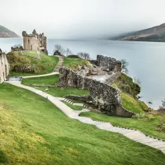 Ruinas de un castillo en una colina verde junto a un lago, ideal para un viaje a Escocia 7 días.