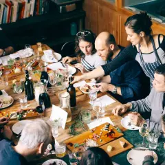 Gente disfrutando de una comida compartida en Barcelona. Una mesa llena de platos, botellas y copas.