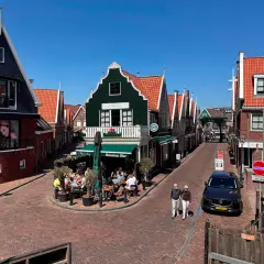 Un paseo por un pueblo holandés con casas de tejados rojos y fachadas coloridas. Un lugar ideal que ver en Holanda, con gente disfrutando en una terraza.