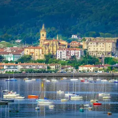 Vista de Hondarribia que ver: un puerto con veleros y barcos, y al fondo la iglesia y edificios históricos.