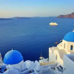 Iglesias blancas con cúpulas azules y el mar Egeo azul profundo. Un crucero navega en la distancia. ¡Imprescindible que ver en Santorini!