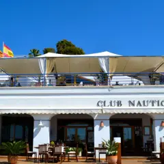 Club Náutico Moraira, ideal para comer en Moraira con vistas al mar. Banderas ondean bajo el sol.