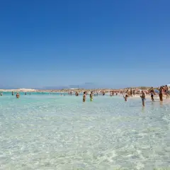 Gente disfrutando de las **mejores playas de Formentera**, con aguas cristalinas y arena blanca bajo un cielo azul.