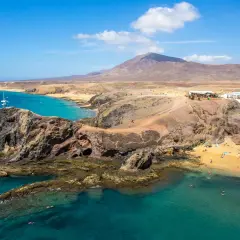 Costa de Lanzarote con playas doradas, aguas turquesas y un restaurante en la colina. ¡Perfecto para tu plan de Lanzarote en 4 días!