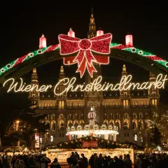Un mercado navideño en Viena, con un arco de luces y un gran lazo rojo. El edificio del ayuntamiento ilumina el fondo.