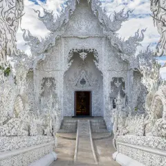 El Wat Rong Khun, un templo blanco deslumbrante en Tailandia, exhibe intrincadas esculturas de dragones y motivos ornamentados bajo un cielo azul.
