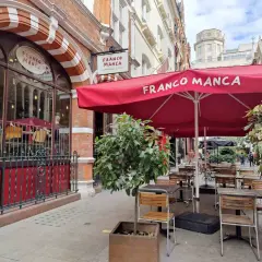 Franco Manca, un lugar ideal donde comer en Londres, con mesas al aire libre bajo sombrillas rojas.