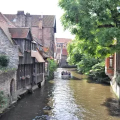 Un paseo en barco por los canales es ideal para ver Brujas en un día. Casas antiguas y árboles frondosos bordean el agua.