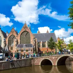 Gente disfrutando de un free tour en Ámsterdam, cruzando un puente sobre un canal frente a una iglesia histórica.