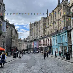 Calle adoquinada de Edimburgo, con edificios históricos y coloridas fachadas. Gente paseando, ideal para un **free tour Edimburgo**.
