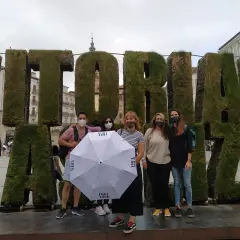 Grupo posa frente a letras gigantes de césped que dicen "VITORIA". Sostienen un paraguas blanco con el logo "FREE TOUR".