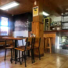 Mesas de madera y sillas listas para comer en Pontedeume. Barra con botellas y vasos, y un mural de la ciudad.
