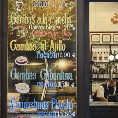 Cartel de un restaurante con menú de gambas y langostinos, y un camarero detrás del mostrador.