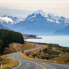 Carretera serpenteante hacia montañas nevadas y un lago turquesa. Impresionantes vistas de Nueva Zelanda que ver.