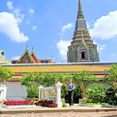 Disfrutando de un free tour en Bangkok, una mujer posa frente a templos tailandeses y pagodas ornamentadas bajo un cielo azul.