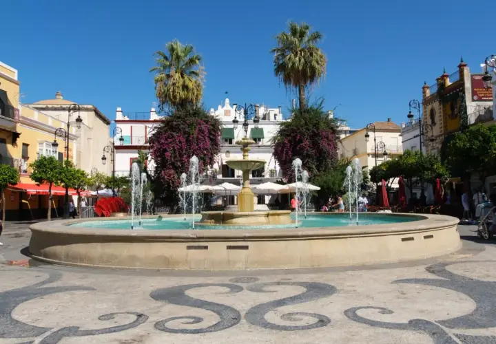Fuente en plaza con palmeras y edificios blancos, ideal para saber qué ver en Sanlúcar de Barrameda.