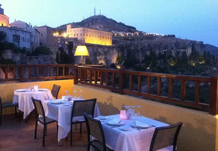 Mesas puestas en terraza con vistas a la ciudad iluminada. Un lugar ideal donde comer en Cuenca al anochecer.