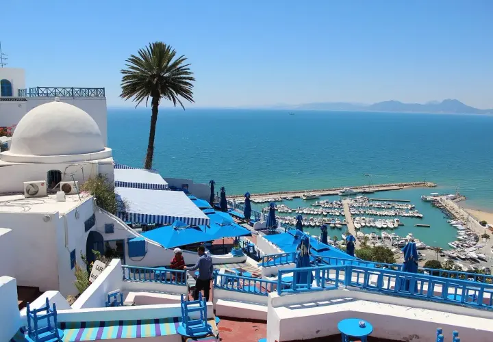 Vista de un puerto deportivo y el mar azul desde un café con cúpulas blancas y sombrillas azules. ¡Un sueño para viajar a Túnez!