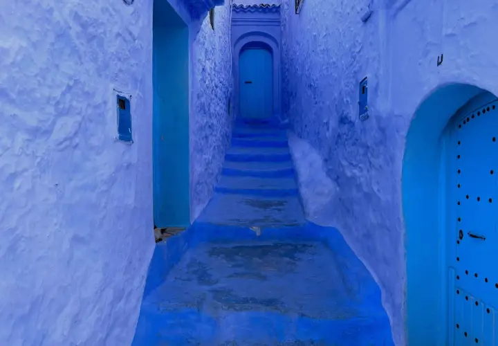 Callejón azul en Chefchaouen, con escalones que suben hacia una puerta. A pesar de su belleza, Chefchaouen es peligroso para los que se pierden en sus laberintos.
