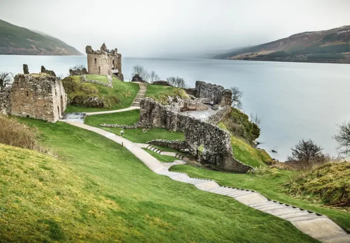 Ruinas de un castillo en una colina verde junto a un lago, ideal para un viaje a Escocia 7 días.