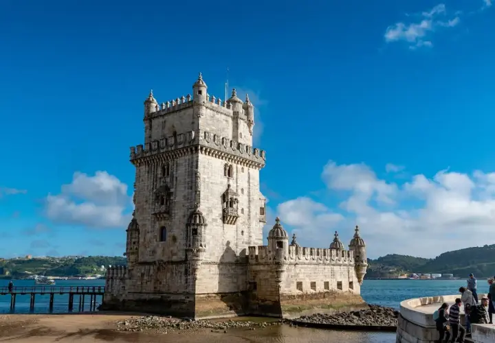 Torre de Belém, un sitio histórico perfecto para un free tour Lisboa. El cielo azul y el agua reflejan su belleza.