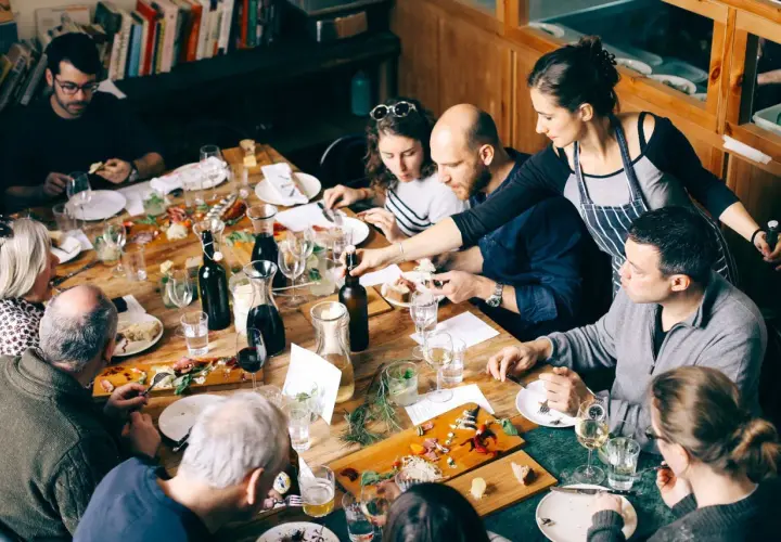 Gente disfrutando de una comida compartida en Barcelona. Una mesa llena de platos, botellas y copas.