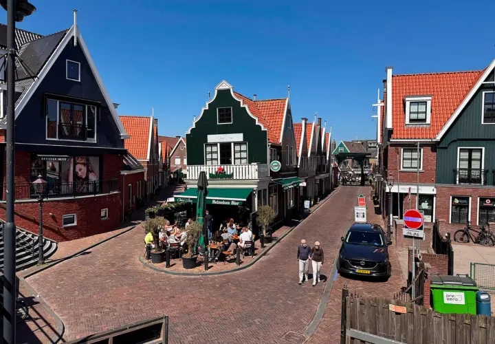 Un paseo por un pueblo holandés con casas de tejados rojos y fachadas coloridas. Un lugar ideal que ver en Holanda, con gente disfrutando en una terraza.