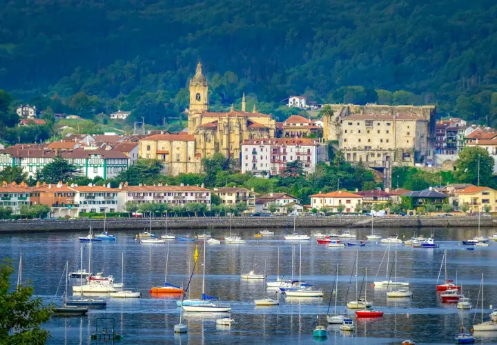 Vista de Hondarribia que ver: un puerto con veleros y barcos, y al fondo la iglesia y edificios históricos.