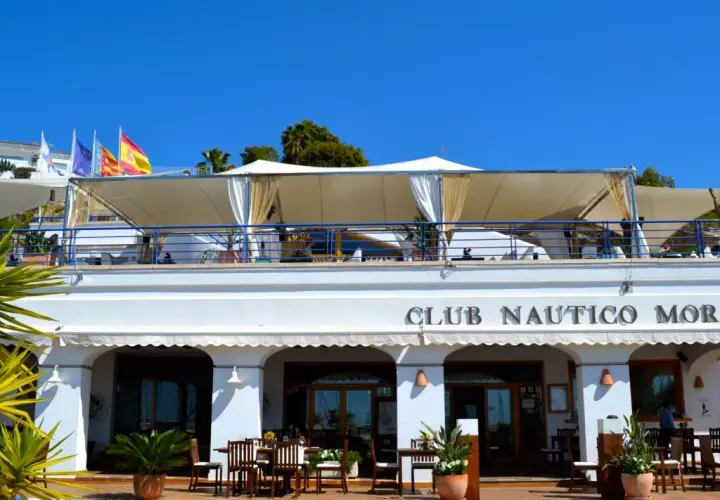 Club Náutico Moraira, ideal para comer en Moraira con vistas al mar. Banderas ondean bajo el sol.