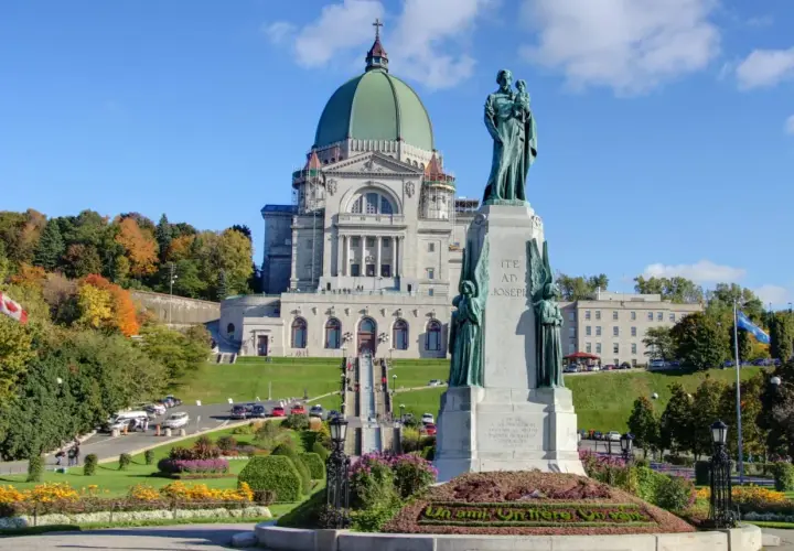 Estátua de São José frente a uma basílica imponente, ideal para visitas guiadas Montreal. Outono com árvores coloridas.