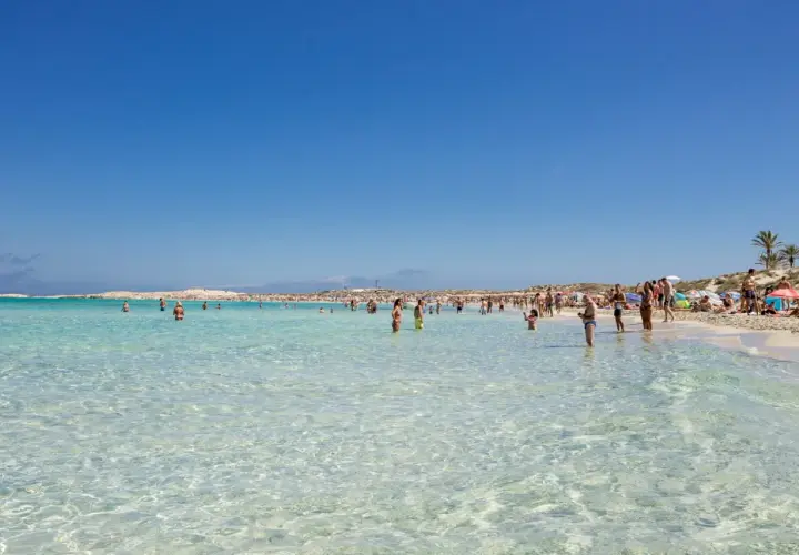 Gente disfrutando de las **mejores playas de Formentera**, con aguas cristalinas y arena blanca bajo un cielo azul.