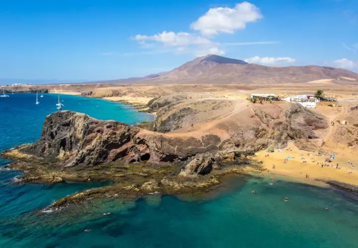Costa de Lanzarote con playas doradas, aguas turquesas y un restaurante en la colina. ¡Perfecto para tu plan de Lanzarote en 4 días!