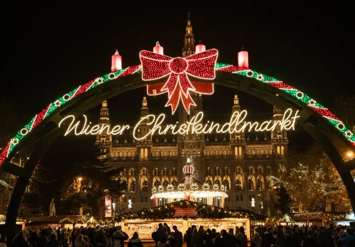 Un mercado navideño en Viena, con un arco de luces y un gran lazo rojo. El edificio del ayuntamiento ilumina el fondo.