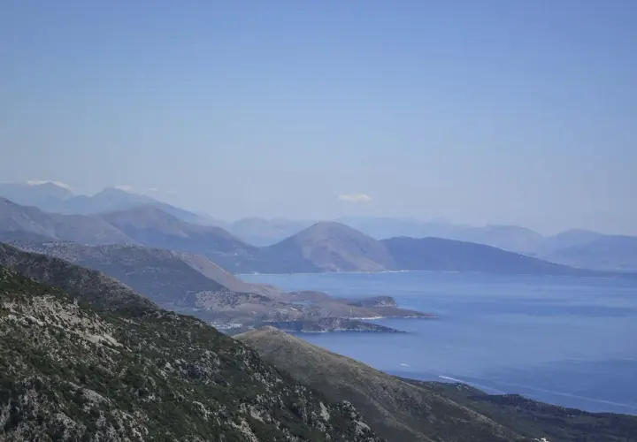 Paisaje montañoso con el mar azul al fondo, ideal para viajar a Albania y disfrutar de vistas espectaculares.