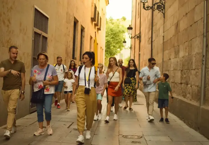 Un grupo disfruta de un free tour en Salamanca, guiado por una mujer con un micrófono, mientras pasean por una calle estrecha y empedrada.