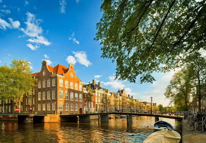 Un día perfecto para viajar a Ámsterdam: casas históricas junto a un canal, puentes y barcas bajo un cielo azul.