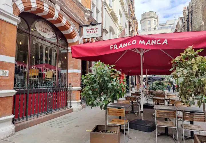 Franco Manca, un lugar ideal donde comer en Londres, con mesas al aire libre bajo sombrillas rojas.