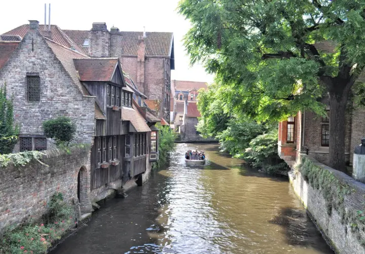 Un paseo en barco por los canales es ideal para ver Brujas en un día. Casas antiguas y árboles frondosos bordean el agua.
