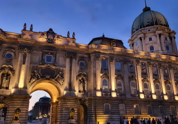 Palacio de Buda iluminado al atardecer, ideal para **free tours Budapest**. Una joya arquitectónica con cúpula verde y detalles ornamentados.