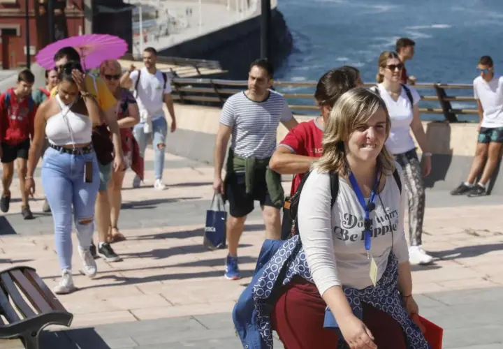 Un grupo de turistas participa en un free tour Gijón, disfrutando del paseo marítimo bajo un sol radiante.
