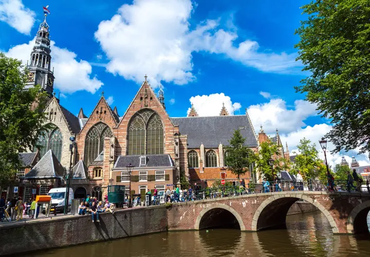 Gente disfrutando de un free tour en Ámsterdam, cruzando un puente sobre un canal frente a una iglesia histórica.