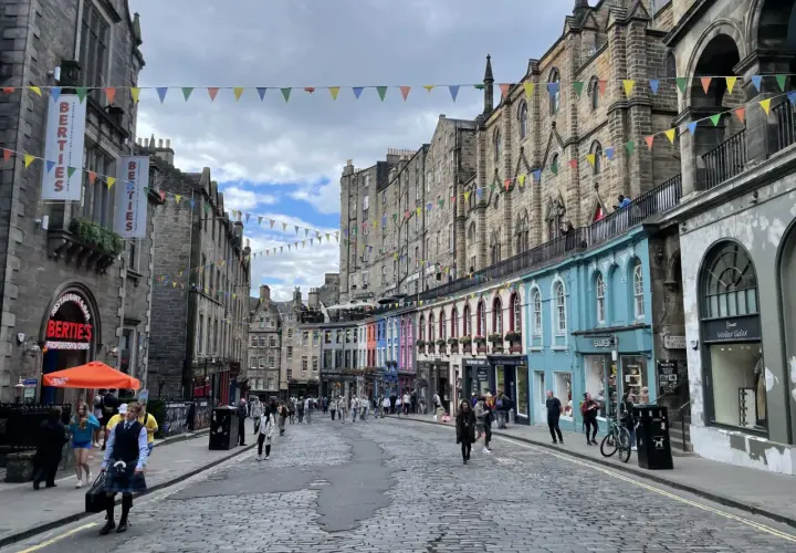 Calle adoquinada de Edimburgo, con edificios históricos y coloridas fachadas. Gente paseando, ideal para un **free tour Edimburgo**.