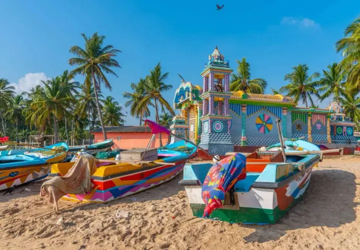 Barcas coloridas en la playa de Sri Lanka, con un templo vibrante al fondo. Es seguro viajar a Sri Lanka y disfrutar de su belleza.