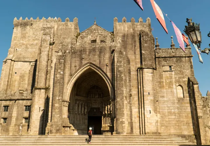 Impresionante Catedral de Tui, un lugar imprescindible que ver en Tui. Fachada de piedra con arco gótico y una persona en las escaleras.