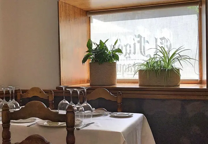 Mesa puesta con copas y plantas en ventana, ideal para saber donde comer en Cáceres.