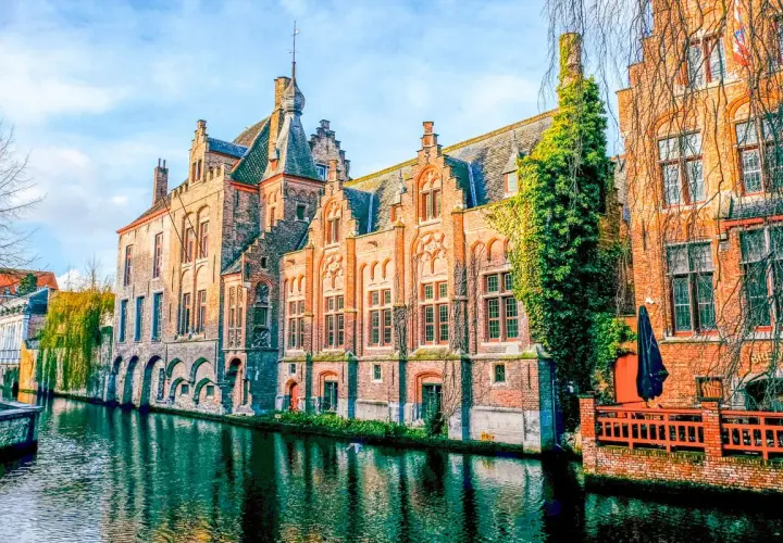 Edificios históricos de ladrillo a lo largo de un canal, reflejando la belleza de Brujas, un viaje inolvidable de Bruselas a Brujas.
