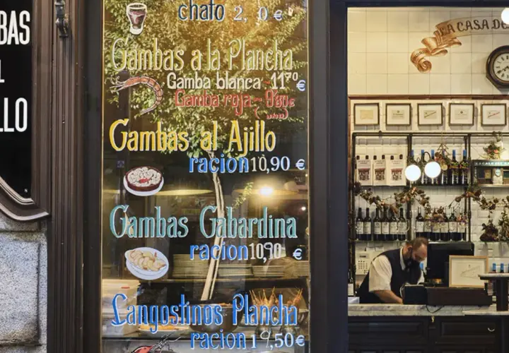 Cartel de un restaurante con menú de gambas y langostinos, y un camarero detrás del mostrador.